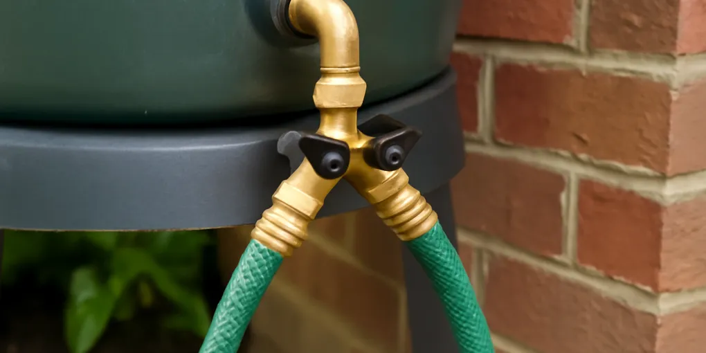 photorealistic brass hose shutoff valve and Y splitter connected to a rain barrel spigot beside a garden bed